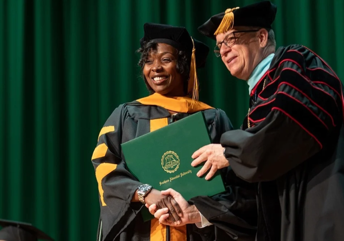 Image of a graduate being handed a diploma on stage.